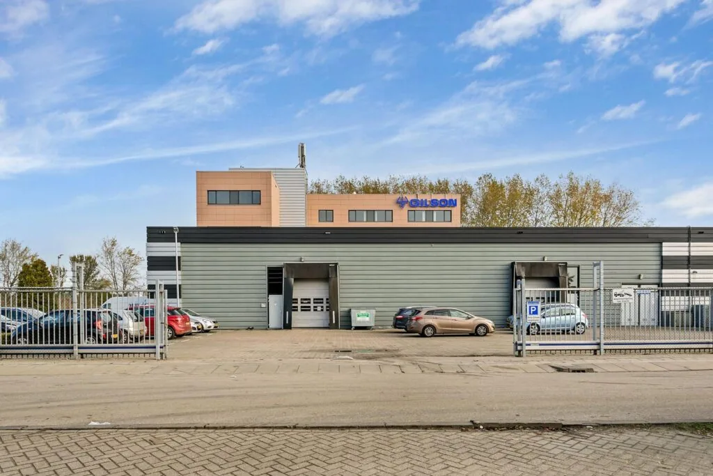 Bedrijfsgebouw van Gilson aan de Laan van ’s-Gravenmade met parkeerplaatsen en laadperrons op de voorgrond.